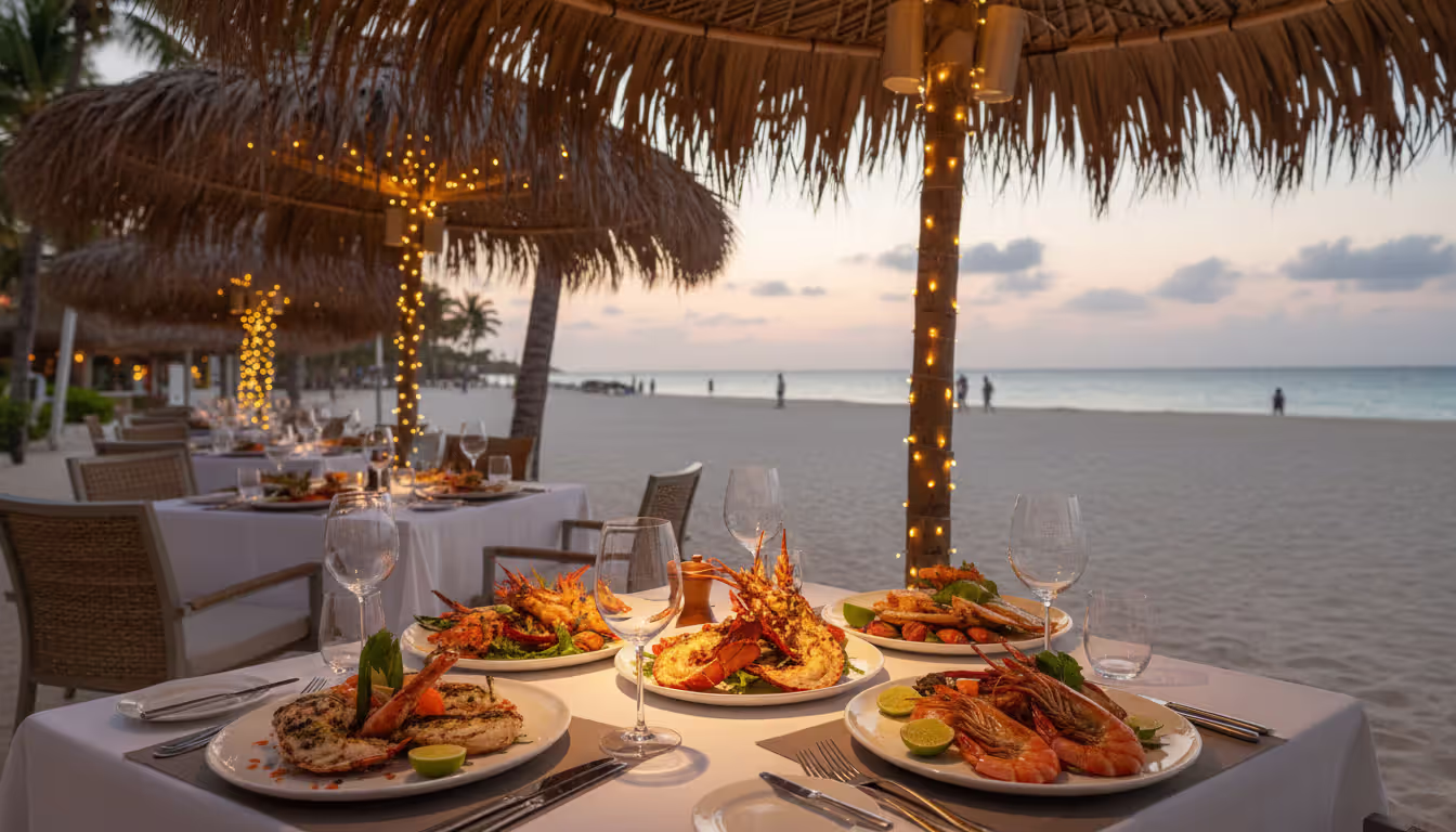 Upscale open-air Caribbean resort restaurant with seafood dishes on a table under a palm leaf canopy with a beach and turquoise sea in the background at evening