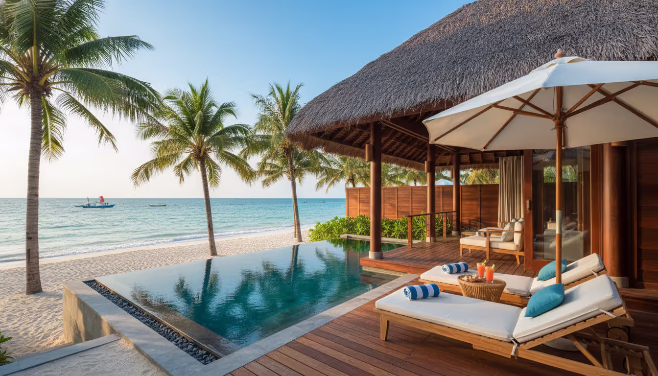 Luxury beachfront villa with thatched roof, private infinity pool, sun loungers on wooden terrace overlooking turquoise sea and white sand in Vietnam