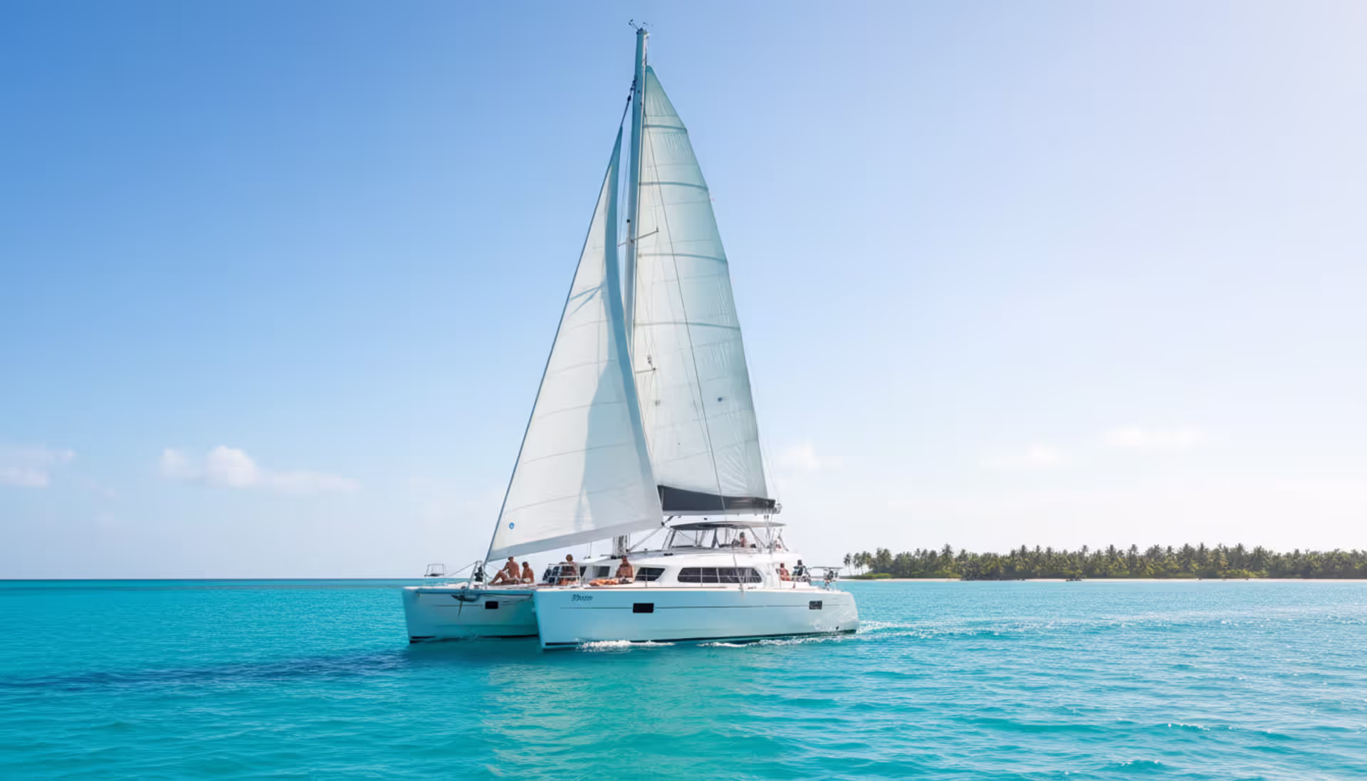 Aerial view of a white catamaran anchored in a turquoise Caribbean bay near a tropical island with palm trees and white sandy beach